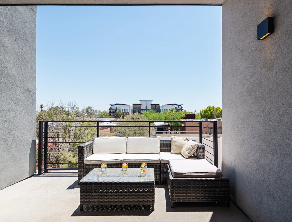 An inviting exterior balcony seating area with a glass-top coffee table and views of the surrounding landscape, ideal for morning coffee, reading, or socializing outdoors. The setting is calm and perfect for gatherings with friends, family, and pets.