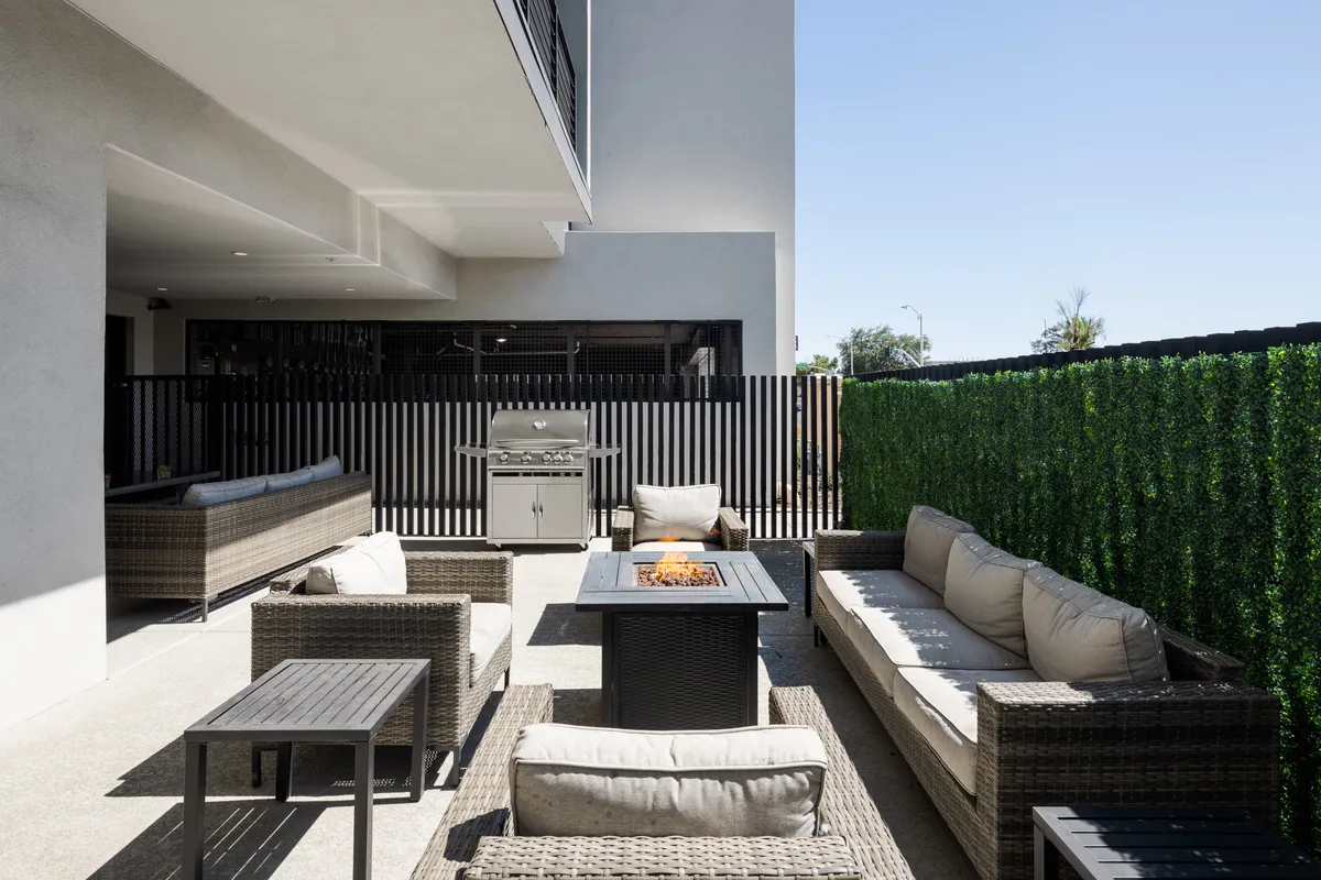 A contemporary outdoor space featuring a fire pit surrounded by seating, a grill station, and a casual lounge area. The mood is warm and community-centered, ideal for barbecues, storytelling, and alfresco meals with friends.