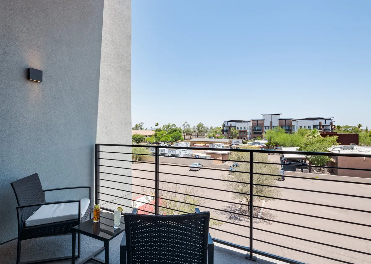 An inviting balcony scene that overlooks the neighborhood, featuring stylish outdoor seating and a decorative table. The space is set up for relaxation, morning coffee, or socializing with friends while taking in the serene outdoor views.