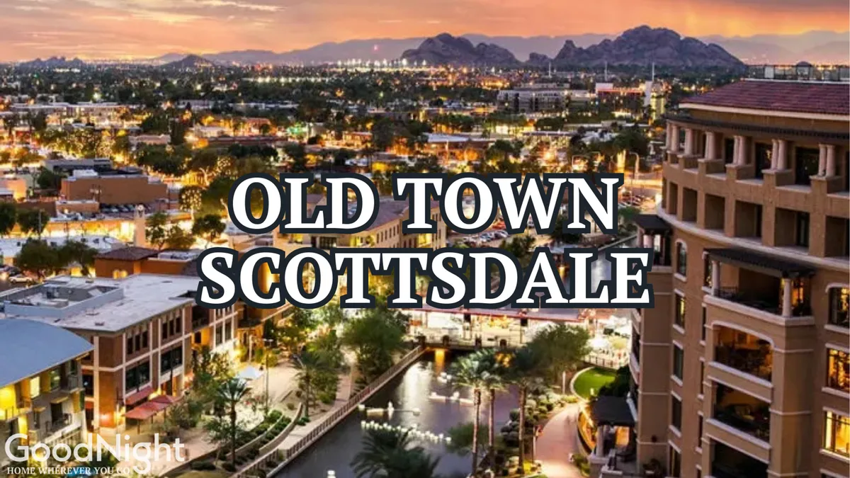 An evening cityscape featuring downtown buildings along a canal, with mountains in the distance and lights illuminating the area. People are seen dining, shopping, and strolling by the water, capturing the inviting nighttime vibe and the array of activities available in the heart of Scottsdale.