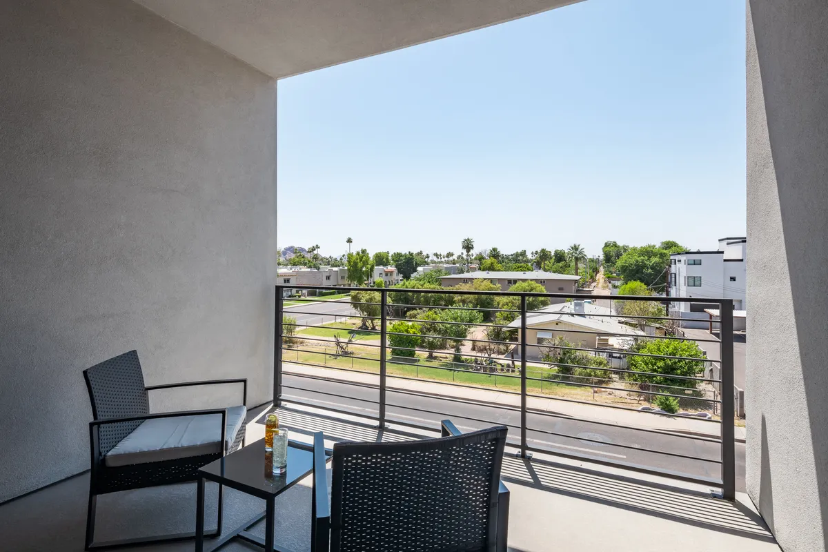 A serene exterior shot featuring a balcony with comfortable seating, potted plants, and a view of the street below. The scene captures the inviting atmosphere for relaxing outdoors with a drink or reading a book, suitable for guests and their pets after a day out.